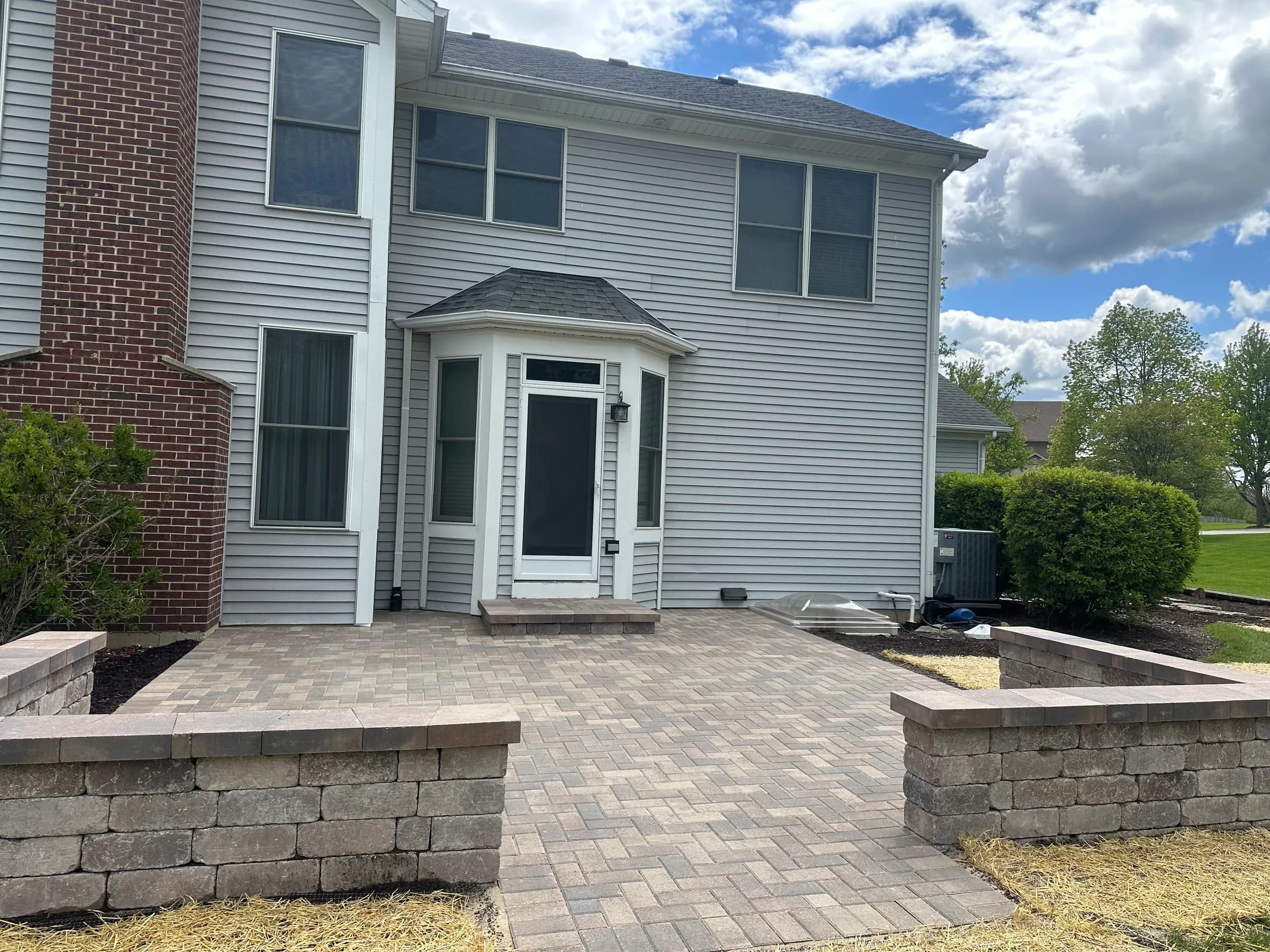 Tan brick paver patio with raised paver planter walls flanking a sunroom entry in Northern Illinois.