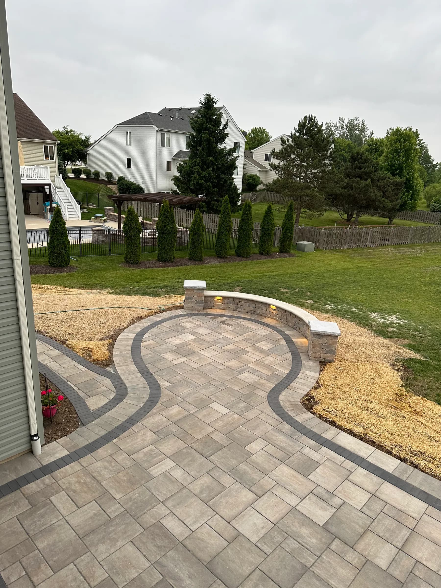 Sweeping paver patio with a contrasting curved border and a lit seat wall with stone columns in Northern Illinois.