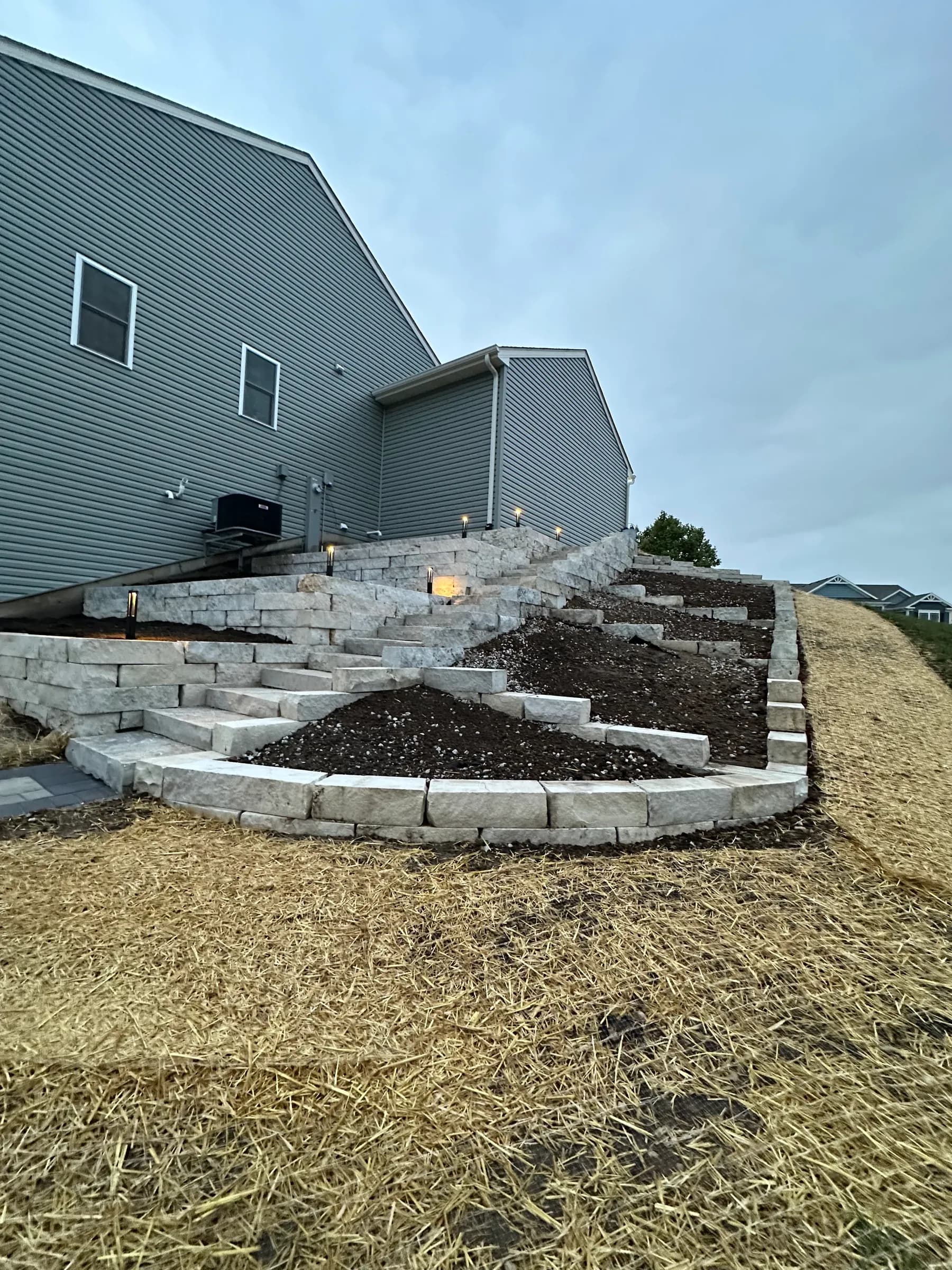 Natural stone raised retaining wall with landscape lighting on a freshly graded and strawed slope.