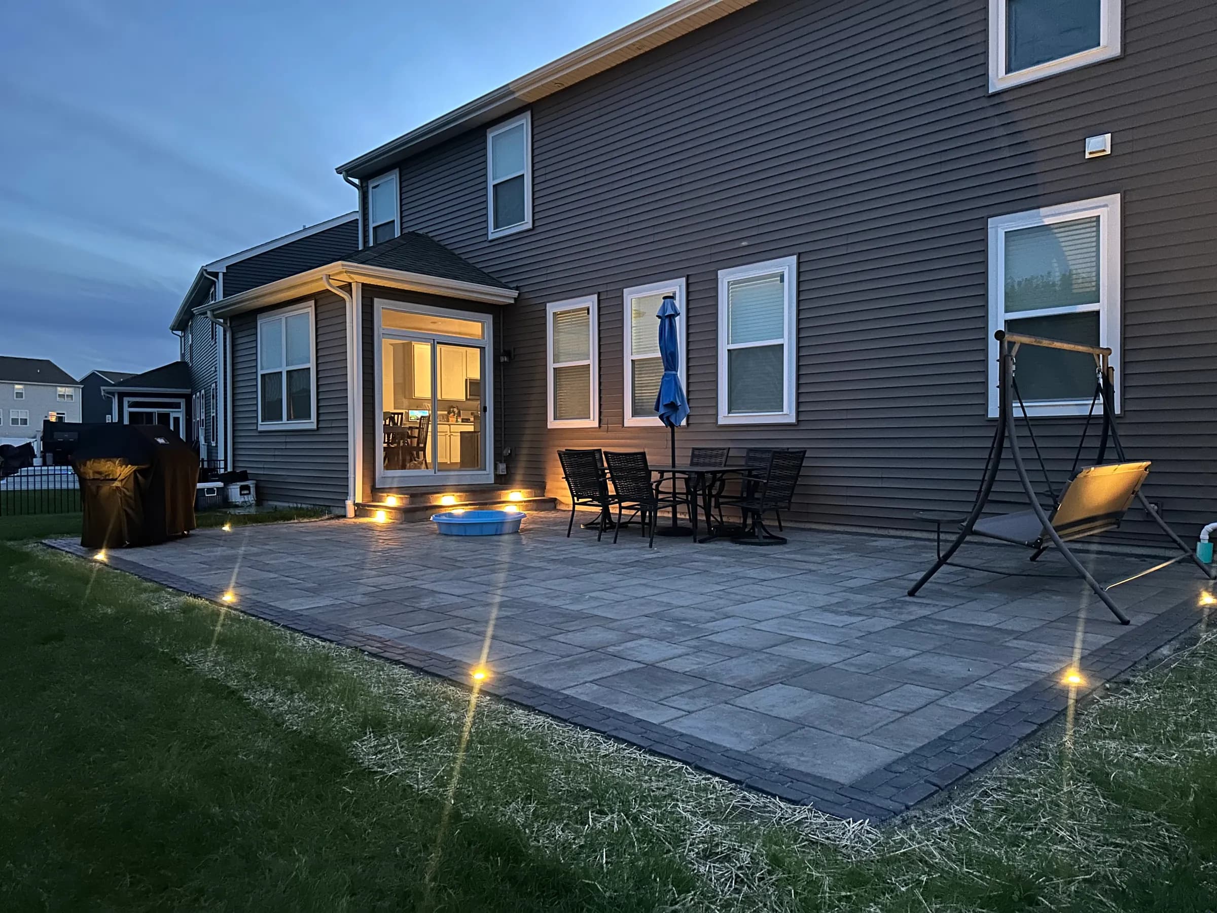 Paver patio at dusk with glowing step lights and in-ground path lighting, installed by E.R. Hardscapes.