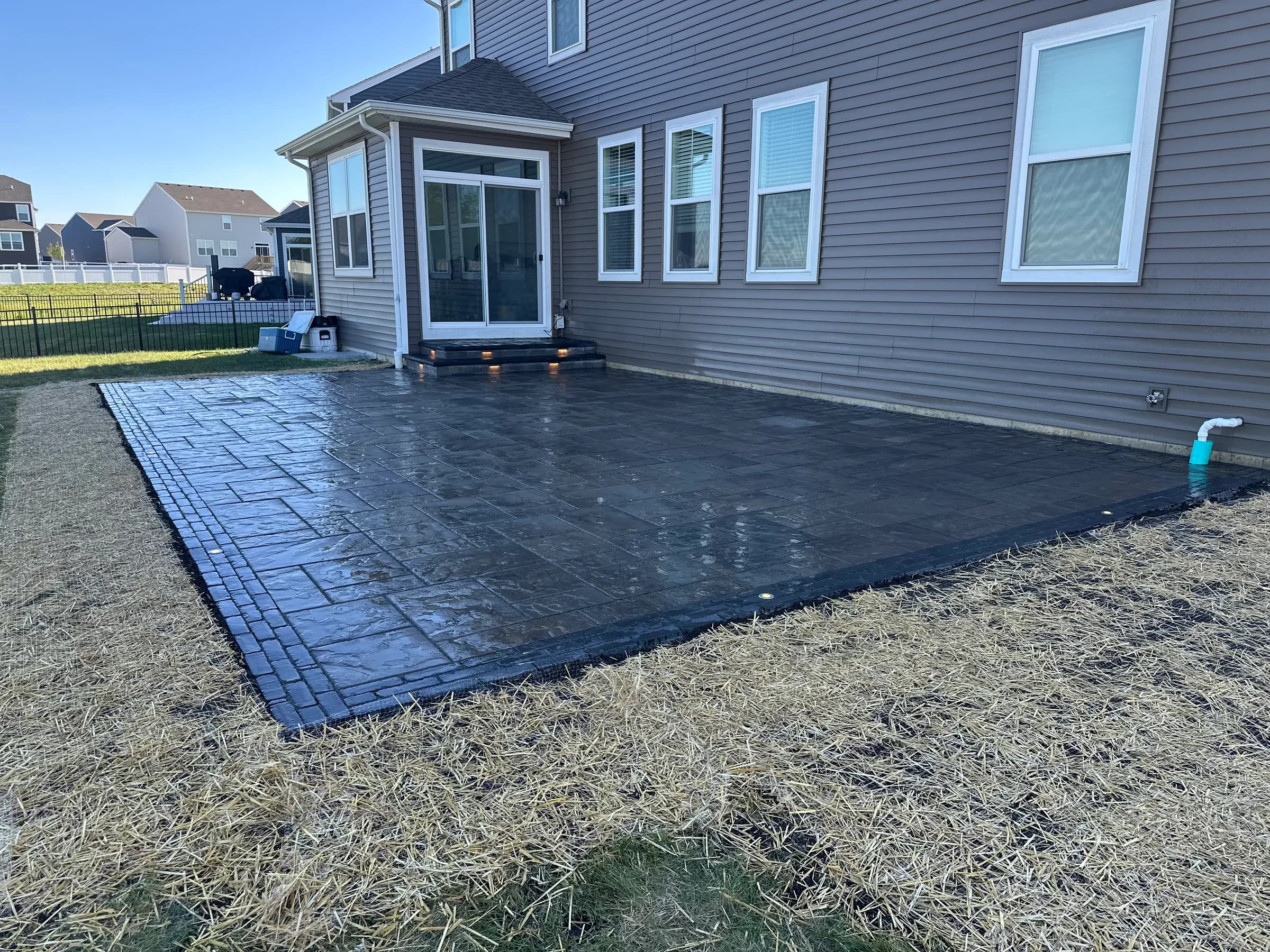 Stamped concrete patio with a brick-pattern border and lit steps installed by E.R. Hardscapes in Northern Illinois.