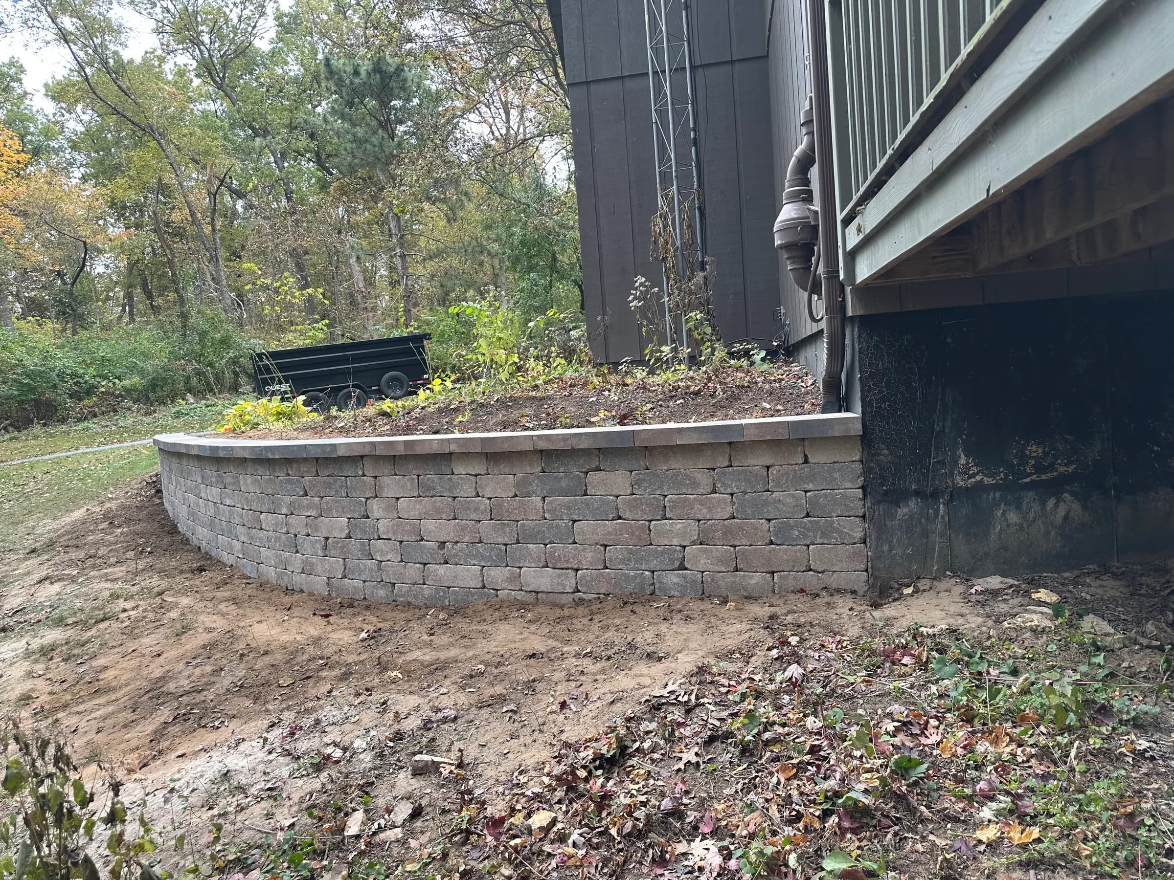 Curved segmental retaining wall with capstones holding back a raised planting bed on a wooded Northern Illinois lot.