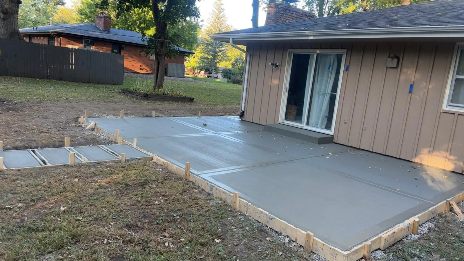 Broom-finish concrete patio wrapping the back of a Northern Illinois home, poured by E.R. Hardscapes with the forms still in place.