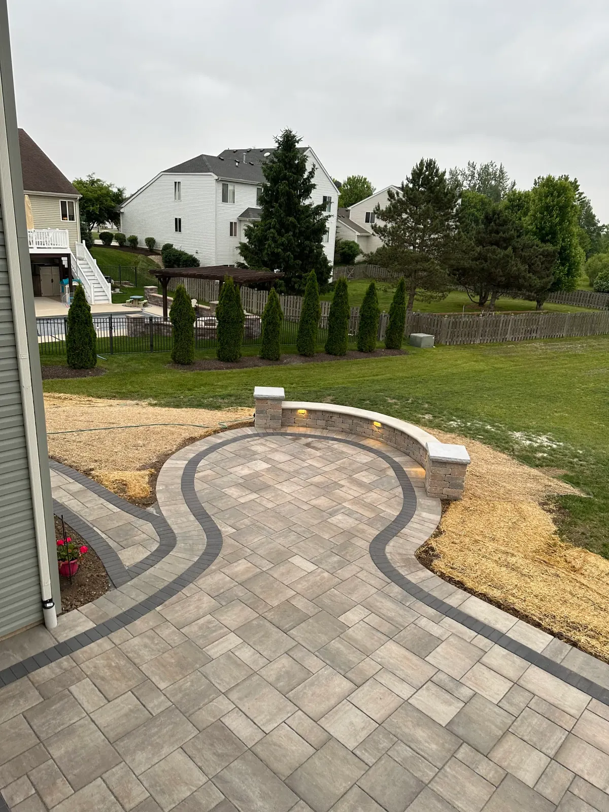 Sweeping paver patio with a contrasting curved border and a lit seat wall with stone columns in Northern Illinois.
