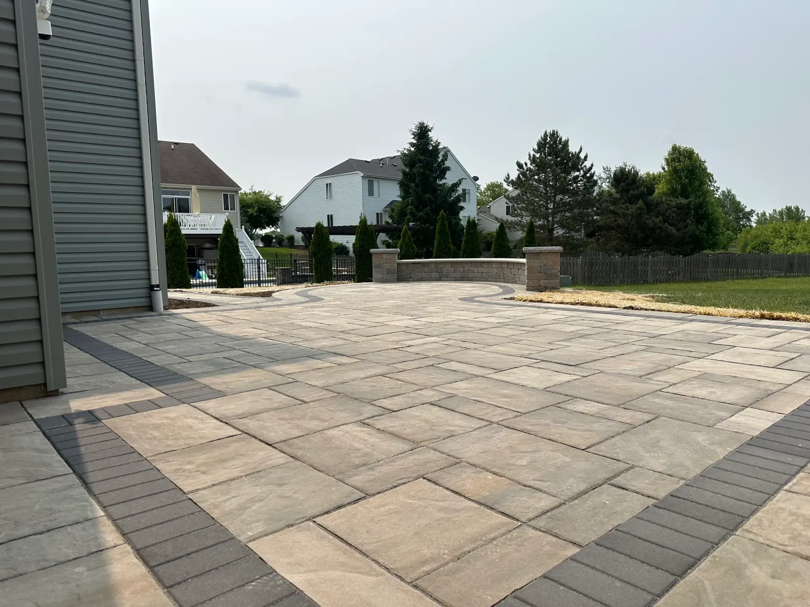 Large tan paver patio with a soldier-course border and a curved seat wall with lit stone columns.