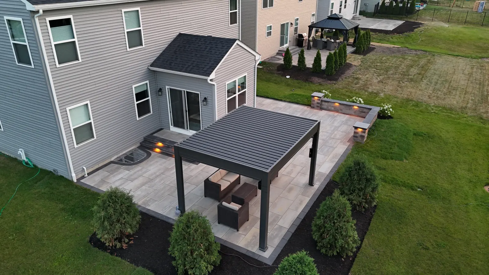 Aerial view of a large-format paver patio with a black louvered pergola and a lit seat wall, built in Northern Illinois.
