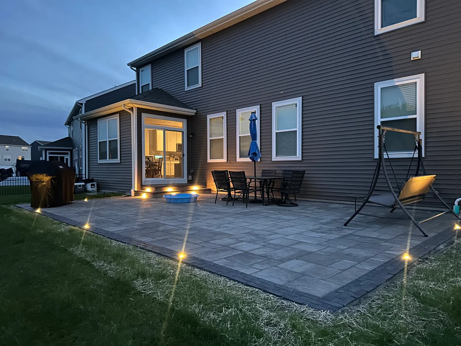 Paver patio at dusk with glowing step lights and in-ground path lighting, installed by E.R. Hardscapes.